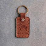 Arizona tan leather keychain debossed with an Australian Shepherd silhouette above THE AUSSIE, on gray concrete