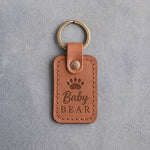 Caramel leather keychain debossed with a small bear cub track above the words Baby BEAR, on gray plaster