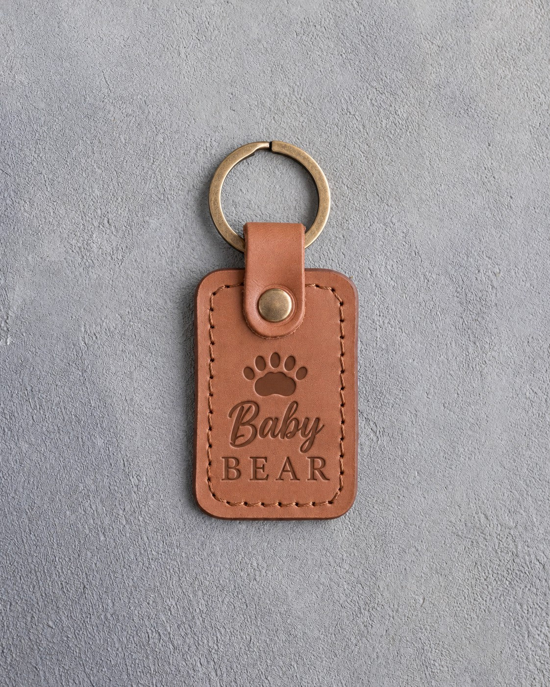 Caramel leather keychain debossed with a small bear cub track above the words Baby BEAR, on gray plaster