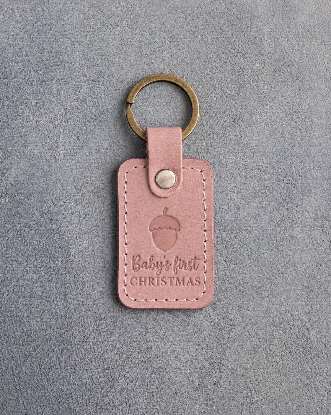 Blush pink leather keychain debossed with a single acorn above Baby's first and CHRISTMAS