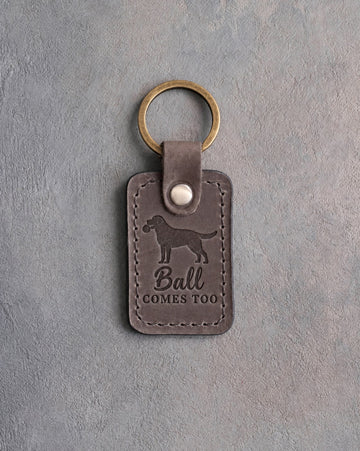 Country gray leather keychain debossed with a Labrador holding a ball in its mouth and the words Ball COMES TOO, on gray concrete