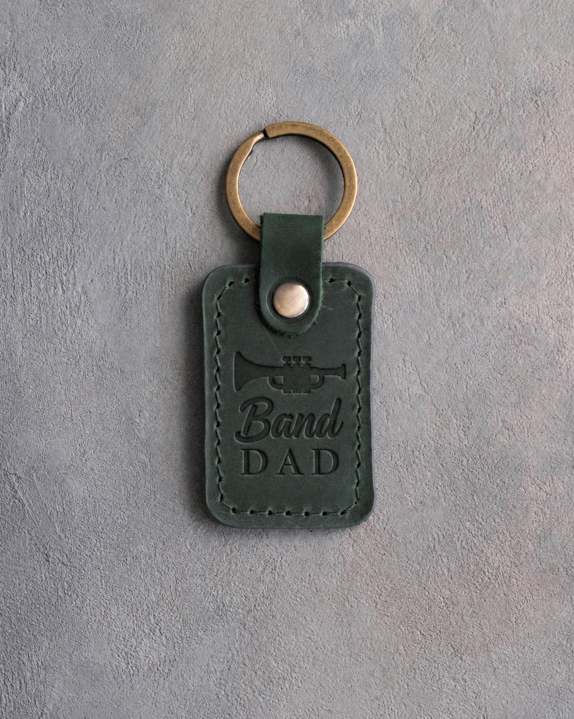 Forest green leather keychain debossed with a trumpet above the words Band DAD, on gray plaster