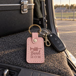 Pink Band Mom keychain on a set of car keys resting on stadium bleachers beside a folded marching band program