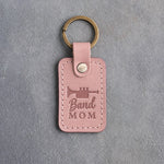 Blush pink leather keychain debossed with a trumpet above the words Band MOM, on gray plaster