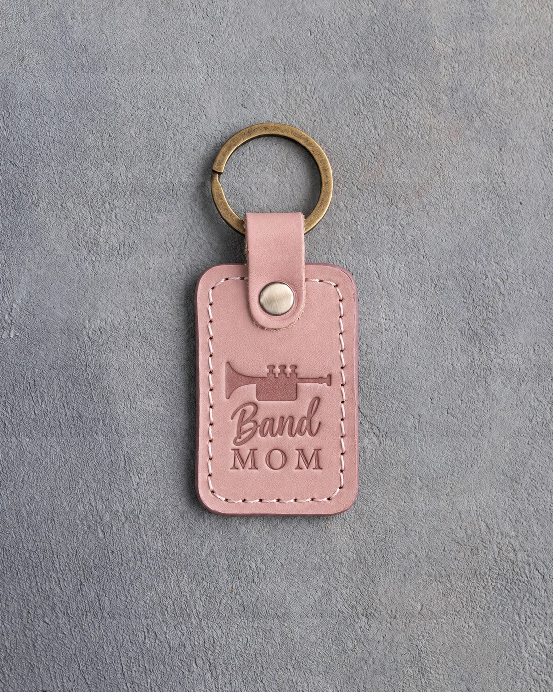 Blush pink leather keychain debossed with a trumpet above the words Band MOM, on gray plaster