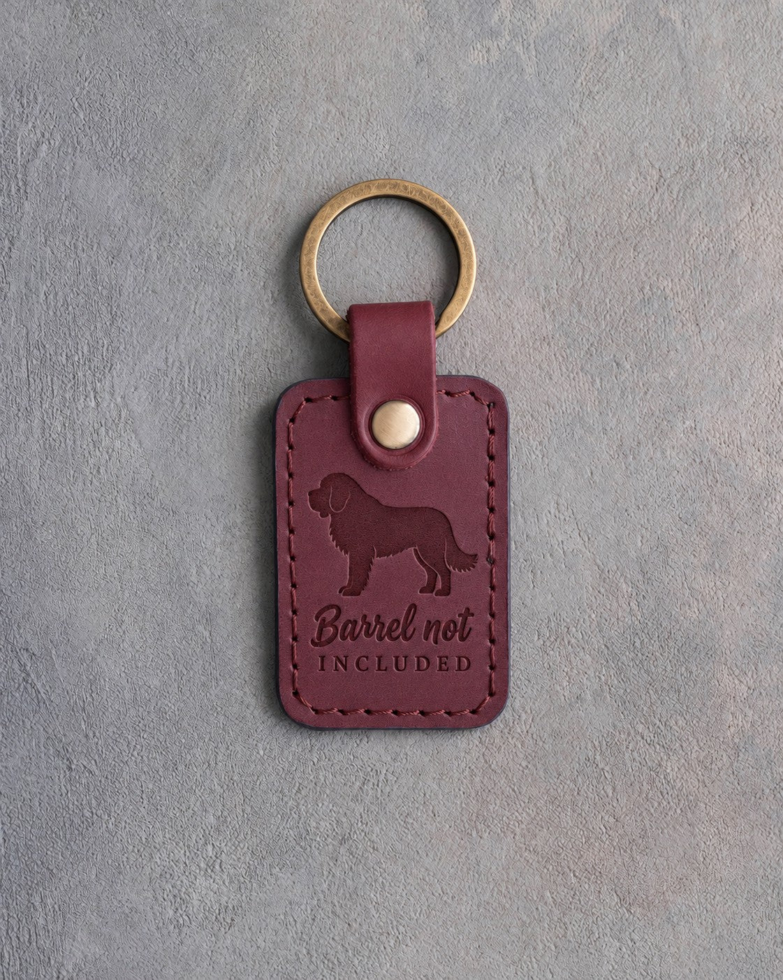 Sangria wine-red leather keychain debossed with a Saint Bernard and the words Barrel not INCLUDED, on gray concrete
