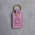 Lilac leather keychain debossed with three barrels in a cloverleaf pattern above Barrel and RACER, on gray plaster