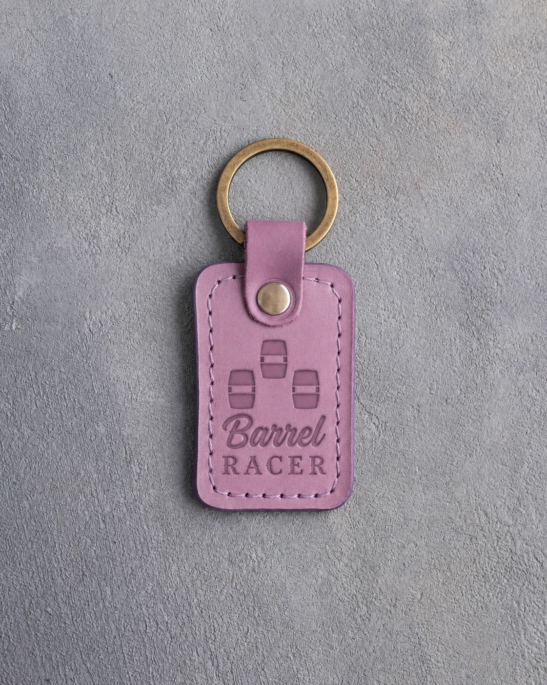 Lilac leather keychain debossed with three barrels in a cloverleaf pattern above Barrel and RACER, on gray plaster
