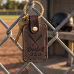 Dark brown Baseball Dad keychain on truck keys resting on a dugout bench beside a worn glove