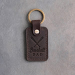 Dark espresso leather keychain debossed with two crossed baseball bats and the words Baseball DAD, on gray plaster