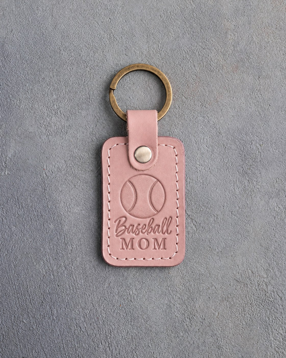 Blush pink leather keychain debossed with a baseball and the words Baseball MOM, on gray plaster