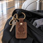 Brown Basketball Dad keychain on keys lying on a driveway beside a basketball at dusk