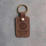Sicilian brown leather keychain debossed with a basketball and the words Basketball DAD, on gray plaster