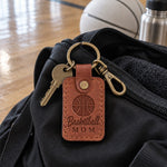 Orange tan Basketball Mom keychain on car keys resting on a gym bleacher beside a water bottle