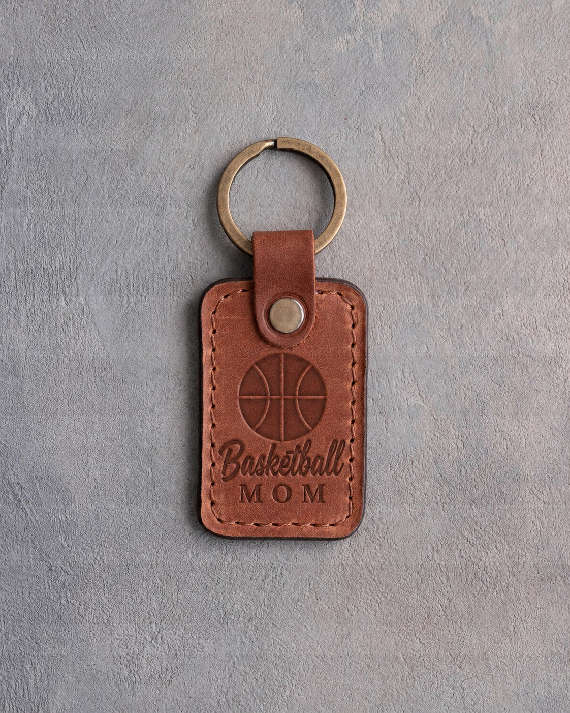 Arizona orange tan leather keychain debossed with a basketball and the words Basketball MOM, on gray plaster