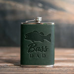 Forest green leather-wrapped hip flask debossed with a largemouth bass above the words Bass DAD, on a wooden table