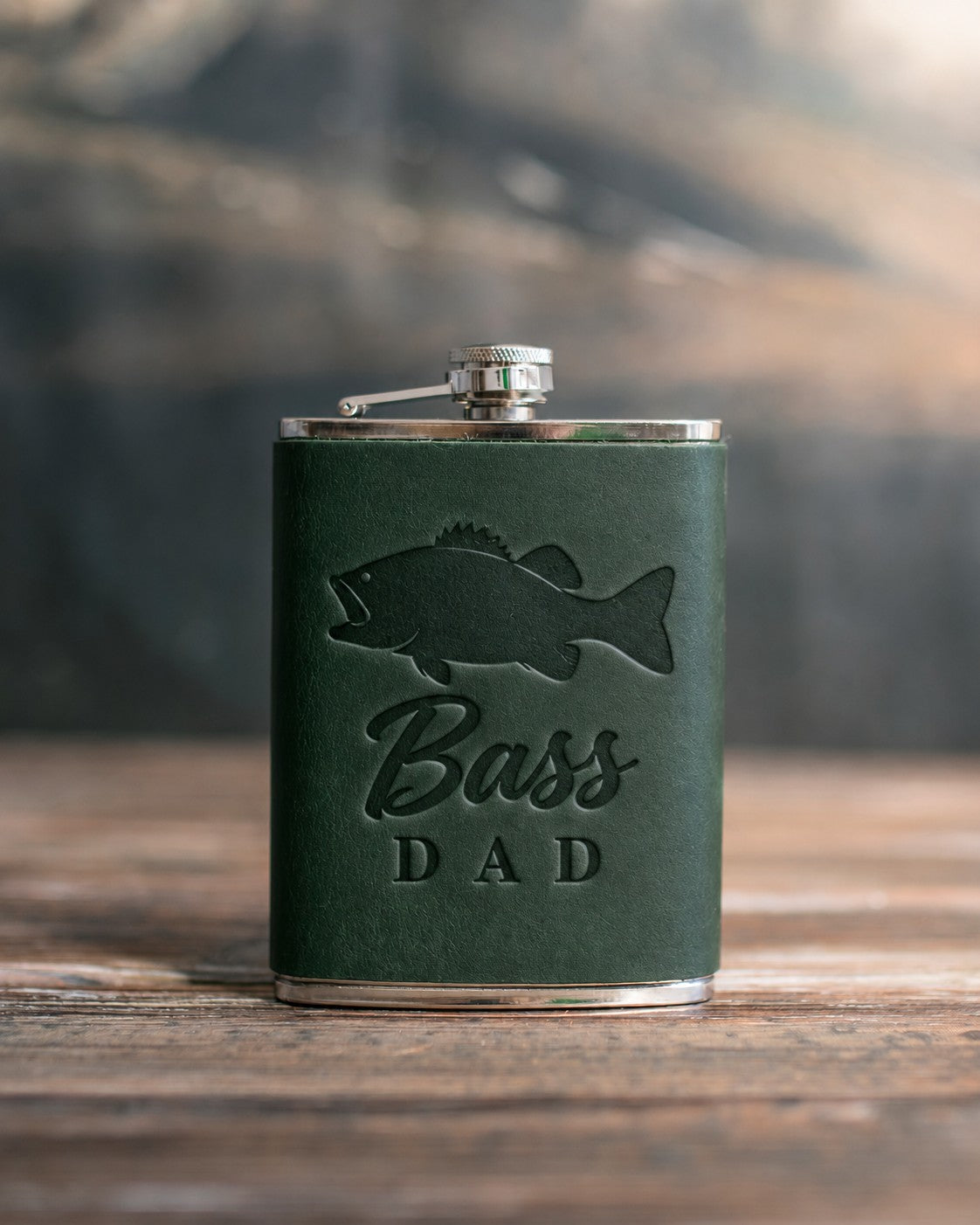 Forest green leather-wrapped hip flask debossed with a largemouth bass above the words Bass DAD, on a wooden table
