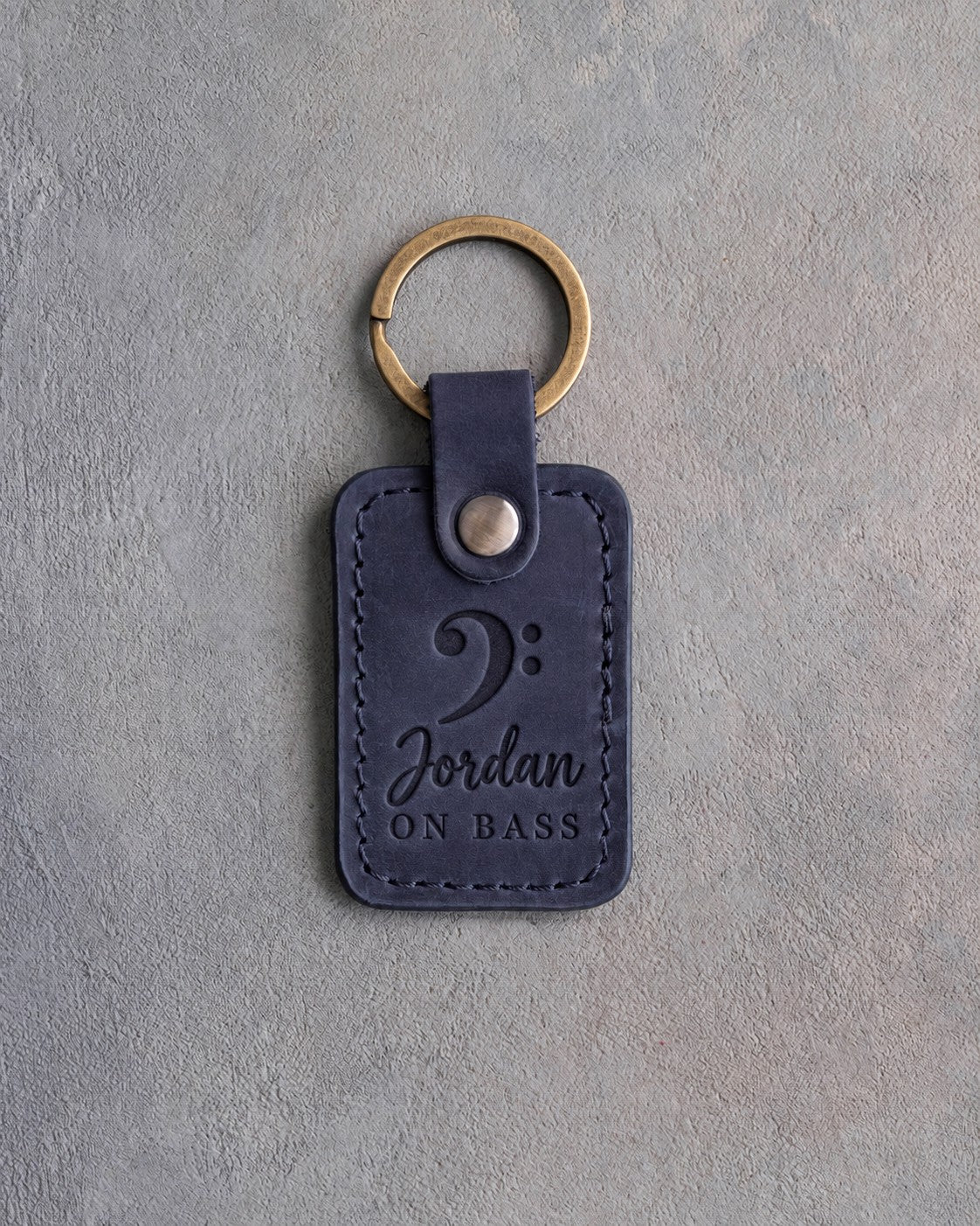 Blueberry navy leather keychain debossed with a bass clef above the name Jordan and ON BASS, on gray plaster