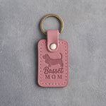 Parisian Blossom pink leather keychain debossed with a Basset Hound silhouette and the words Basset MOM, on gray concrete