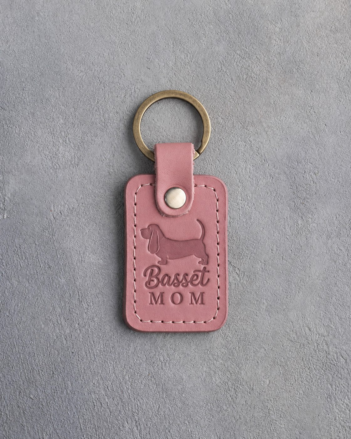 Parisian Blossom pink leather keychain debossed with a Basset Hound silhouette and the words Basset MOM, on gray concrete