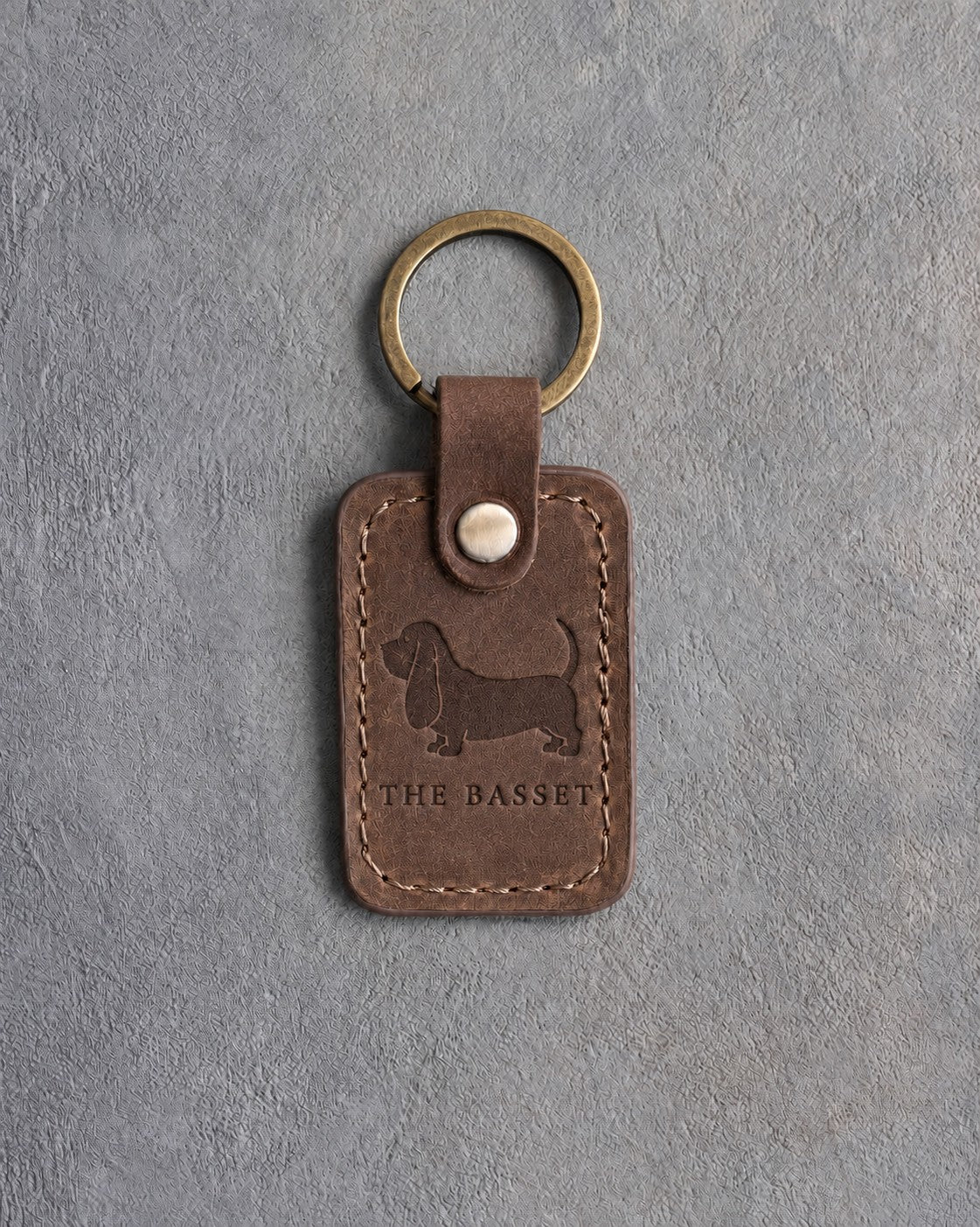 Sicilian brown leather keychain debossed with a Basset Hound silhouette above THE BASSET, on gray concrete