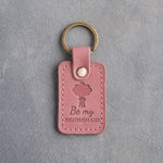 Parisian Blossom pink leather keychain debossed with a hand-tied bouquet above the words Be my BRIDESMAID, on gray concrete