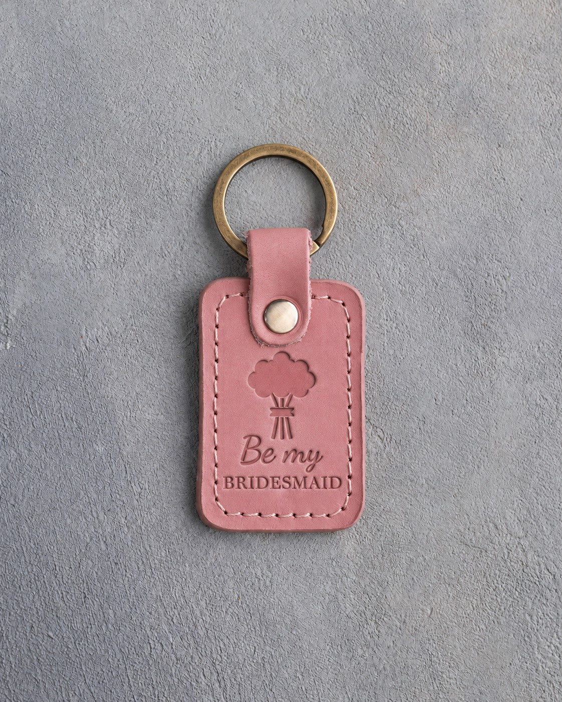 Parisian Blossom pink leather keychain debossed with a hand-tied bouquet above the words Be my BRIDESMAID, on gray concrete