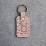 Blush pink leather keychain debossed with a beagle silhouette and the words Beagle GRANDMA, on gray concrete