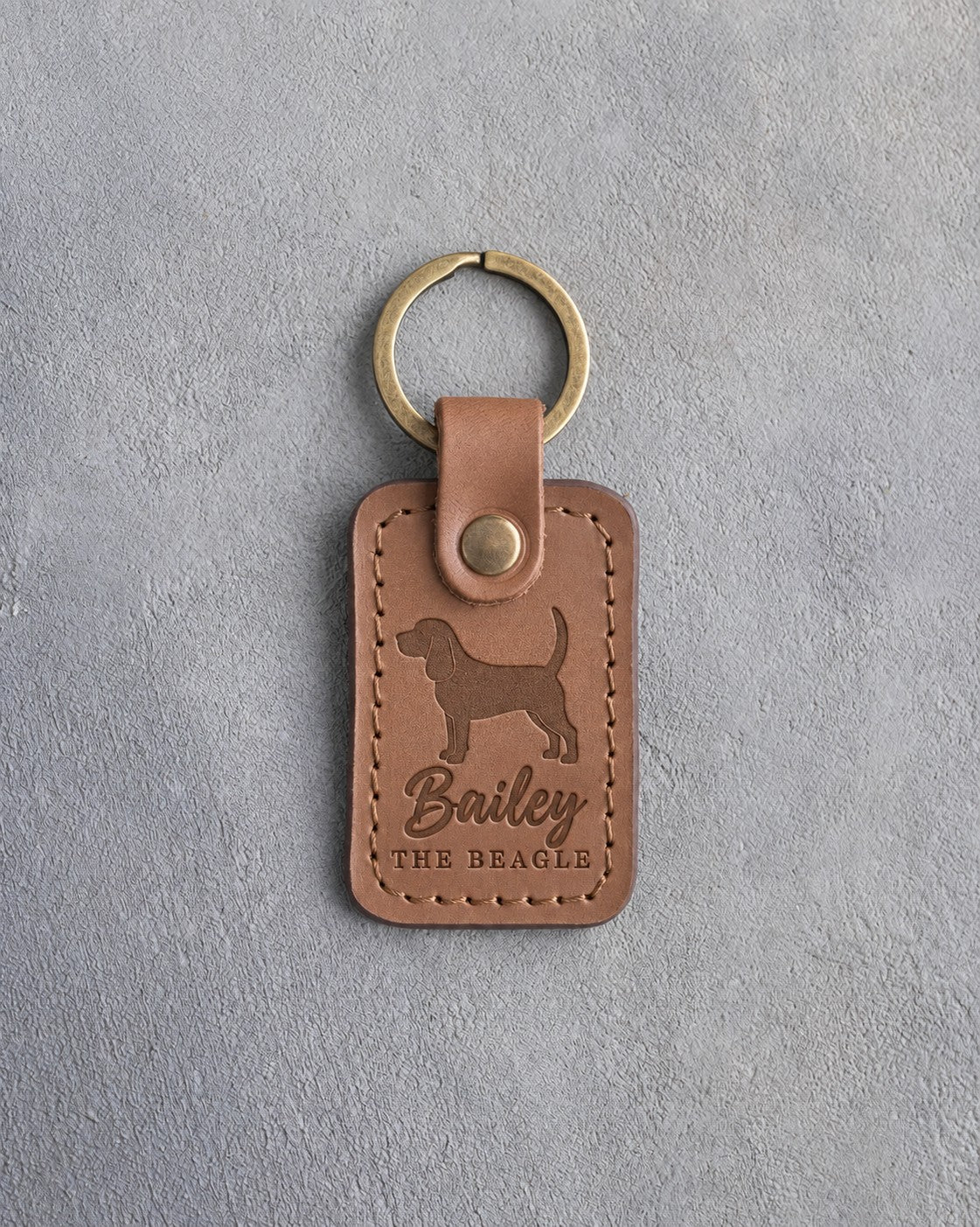 Caramel leather keychain debossed with a Beagle silhouette, the name Bailey and THE BEAGLE, on gray concrete