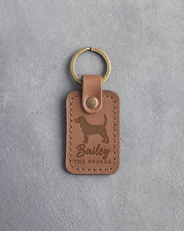 Caramel leather keychain debossed with a Beagle silhouette, the name Bailey and THE BEAGLE, on gray concrete
