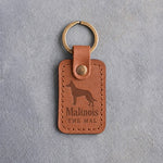 Caramel leather keychain debossed with a Belgian Malinois above Malinois and THE MAL, on gray concrete