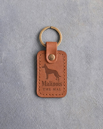 Caramel leather keychain debossed with a Belgian Malinois above Malinois and THE MAL, on gray concrete
