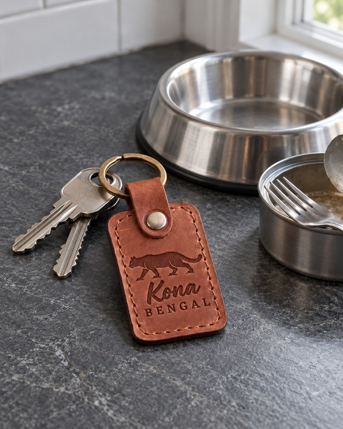 Kona BENGAL keychain in rust tan leather on a wooden shelf beside a climbing rope toy