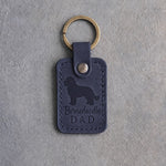 Blueberry navy leather keychain debossed with a Bernedoodle silhouette and the words Bernedoodle DAD, on gray concrete
