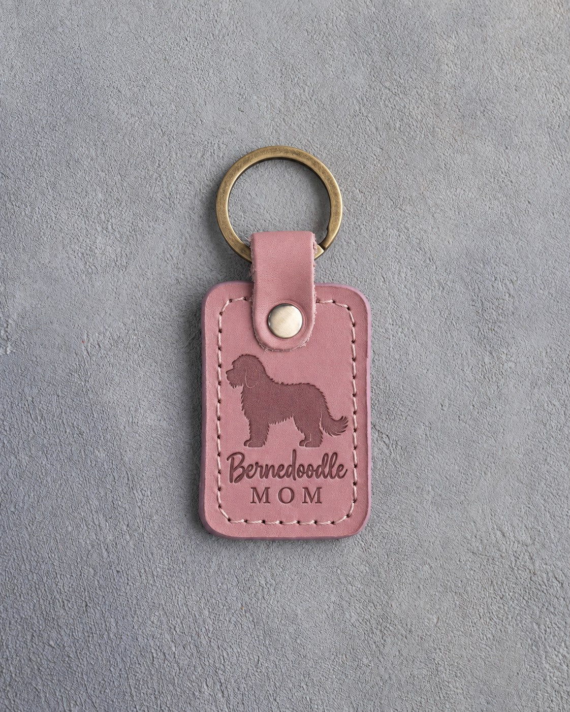 Parisian Blossom pink leather keychain debossed with a Bernedoodle silhouette and the words Bernedoodle MOM, on gray concrete