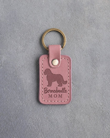 Parisian Blossom pink leather keychain debossed with a Bernedoodle silhouette and the words Bernedoodle MOM, on gray concrete