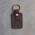 Dark espresso leather keychain debossed with a Bernedoodle silhouette above Doodle love and BERNEDOODLE, on gray concrete