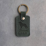 Forest green leather keychain with a debossed Bernese mountain dog and Berner DAD lettering on gray concrete