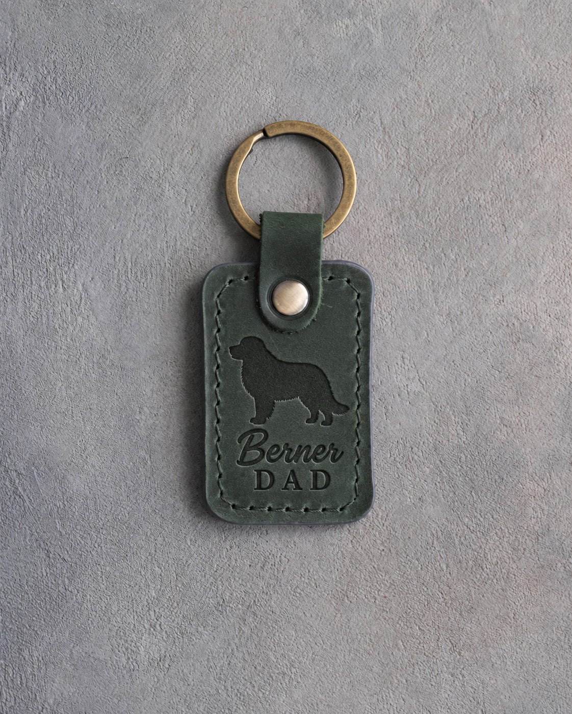 Forest green leather keychain with a debossed Bernese mountain dog and Berner DAD lettering on gray concrete