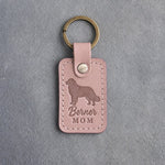 Blush pink leather keychain debossed with a Bernese mountain dog silhouette and the words Berner MOM, on gray concrete