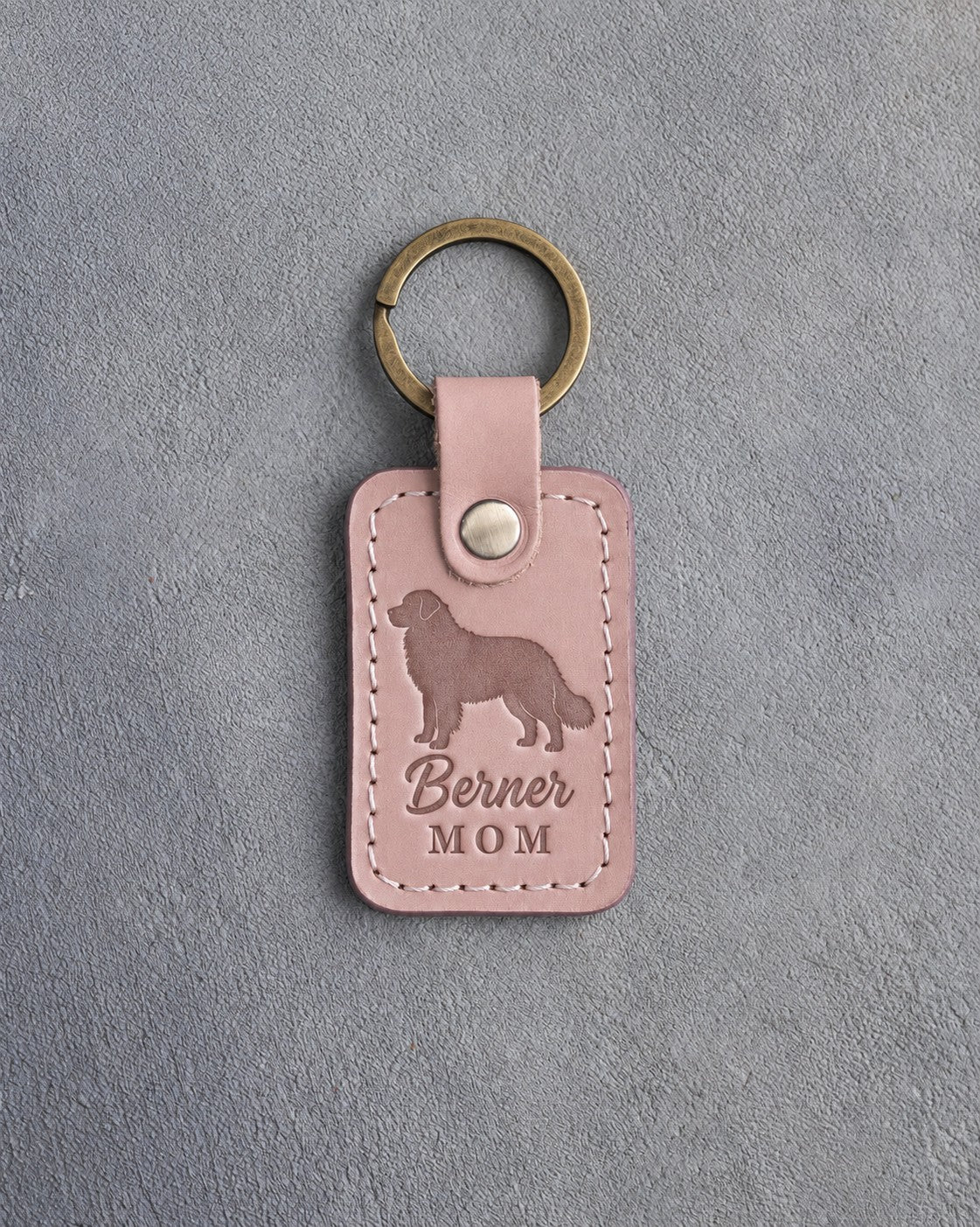 Blush pink leather keychain debossed with a Bernese mountain dog silhouette and the words Berner MOM, on gray concrete