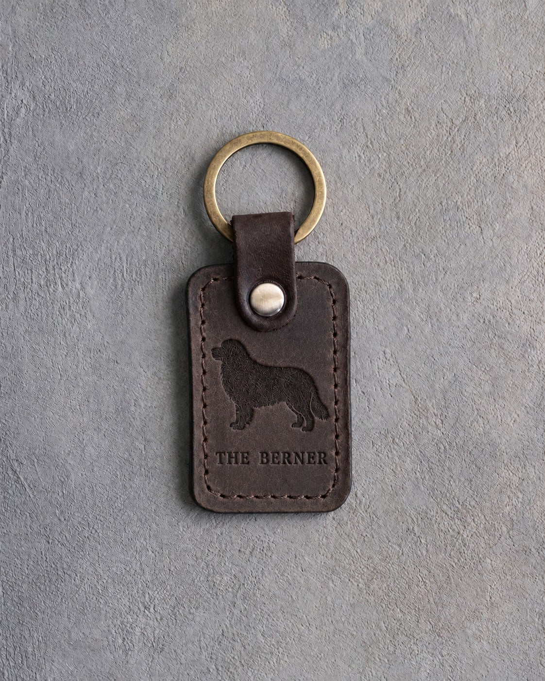 Dark espresso leather keychain debossed with a Bernese mountain dog above THE BERNER, on gray concrete