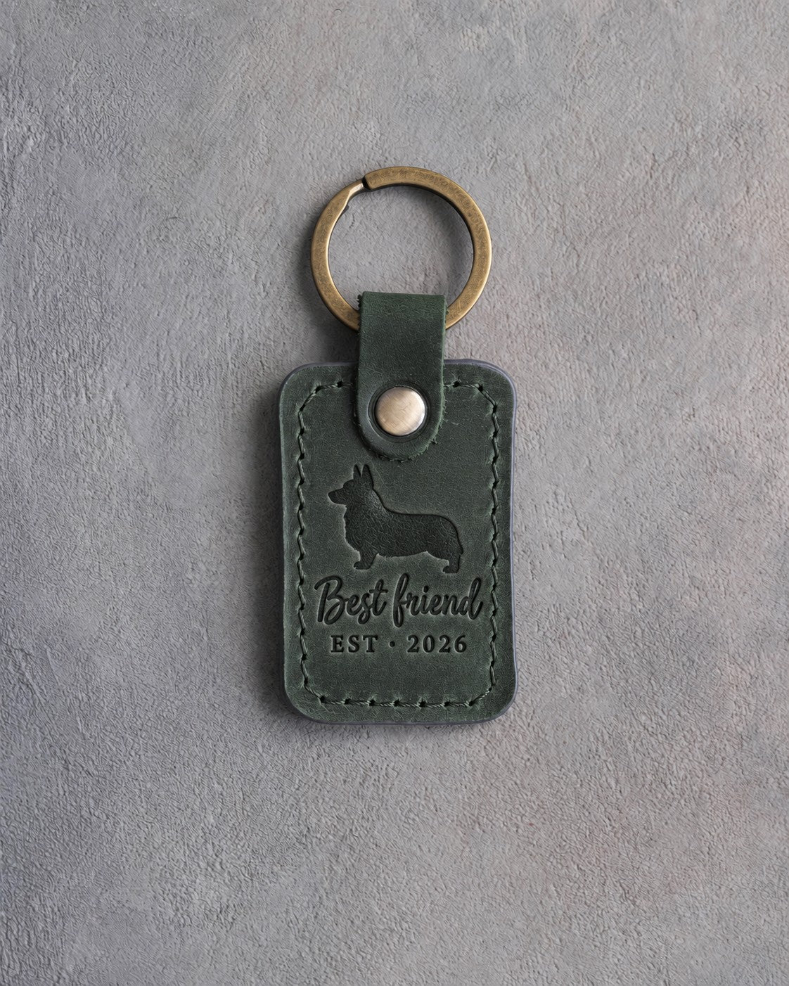 Forest green leather keychain debossed with a corgi and the words Best friend EST · 2026, on gray concrete
