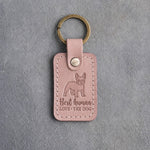 Blush pink leather keychain debossed with a French bulldog above Best human and LOVE · THE DOG, on gray concrete