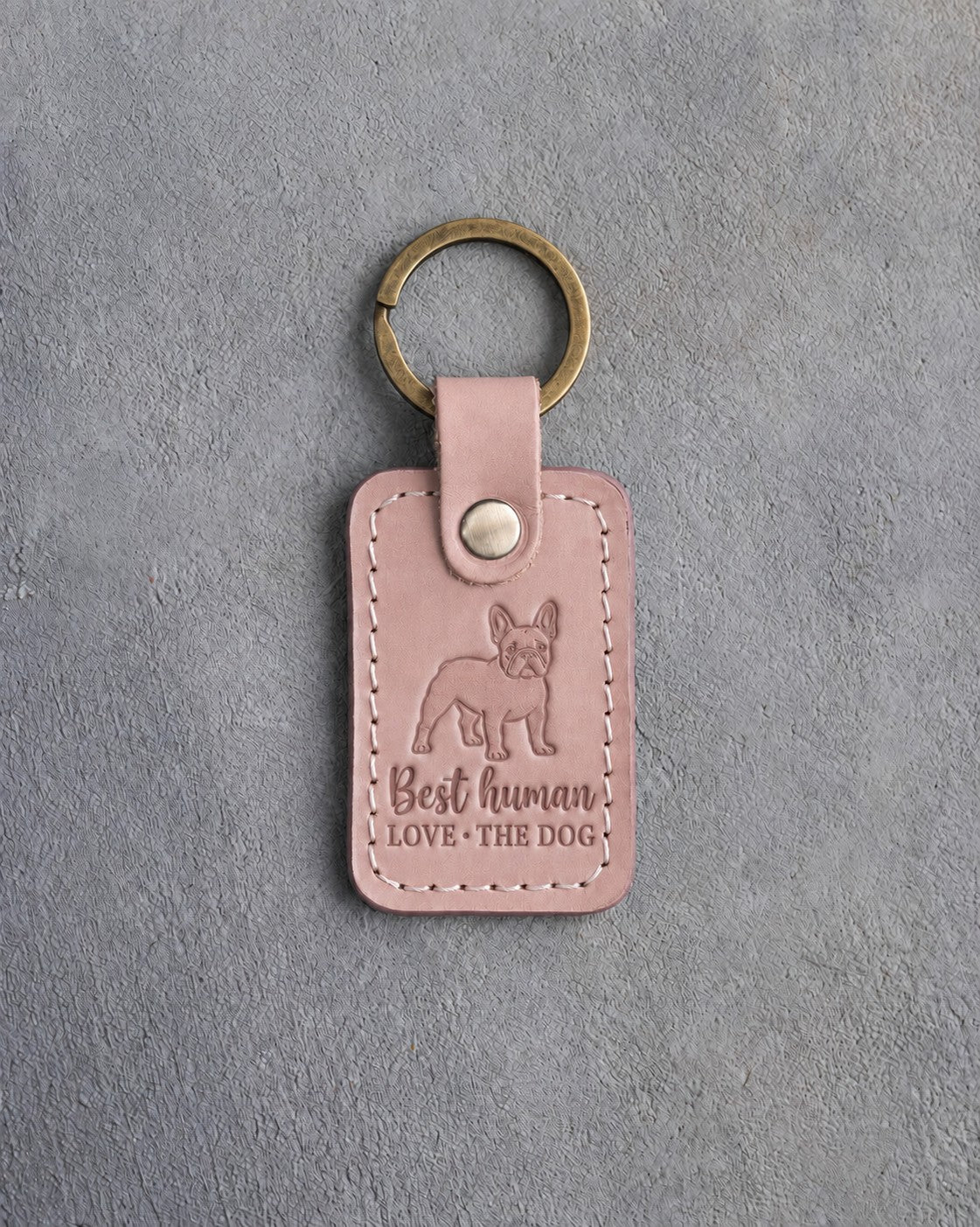 Blush pink leather keychain debossed with a French bulldog above Best human and LOVE · THE DOG, on gray concrete