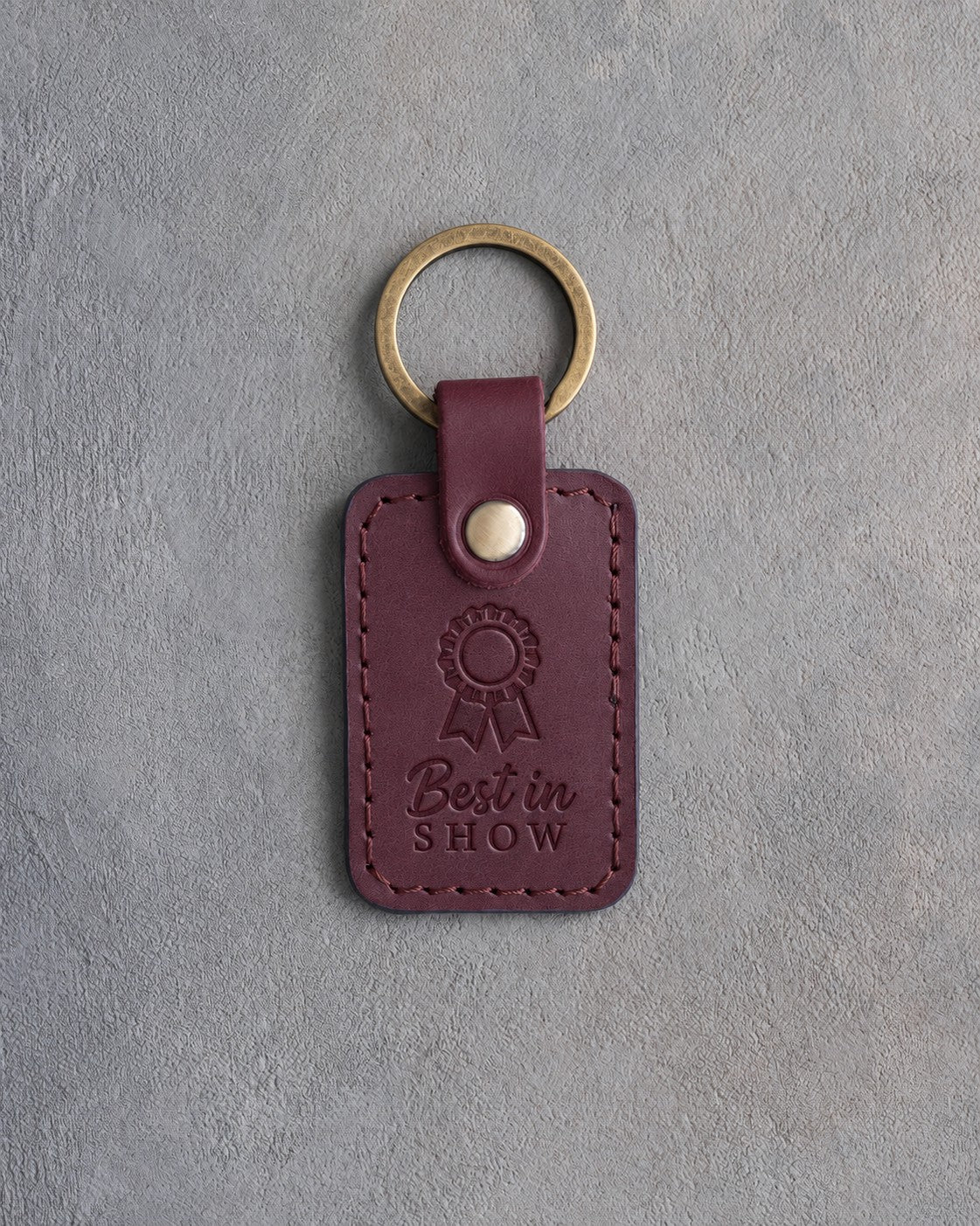 Sangria leather keychain debossed with a show rosette and the words Best in SHOW, on gray concrete