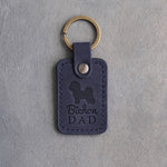 Blueberry navy leather keychain debossed with a Bichon Frise silhouette and Bichon DAD, on gray concrete