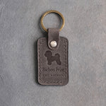 Country gray leather keychain debossed with a powder-puff Bichon Frise above Bichon Frise and THE BICHON, on gray concrete