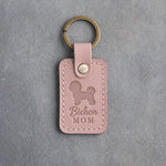 Blush pink leather keychain with a debossed Bichon Frise and the words Bichon MOM on gray concrete