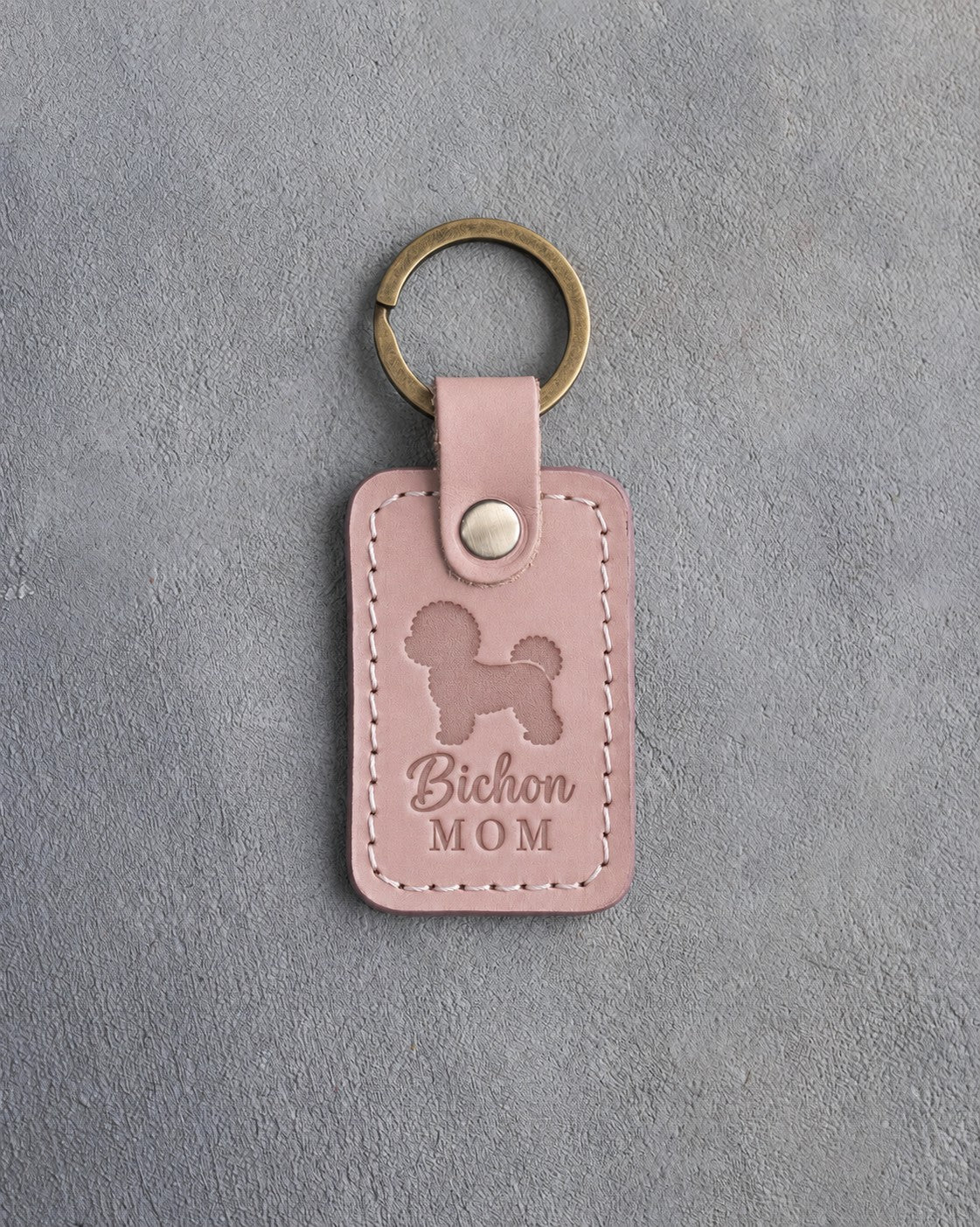 Blush pink leather keychain with a debossed Bichon Frise and the words Bichon MOM on gray concrete